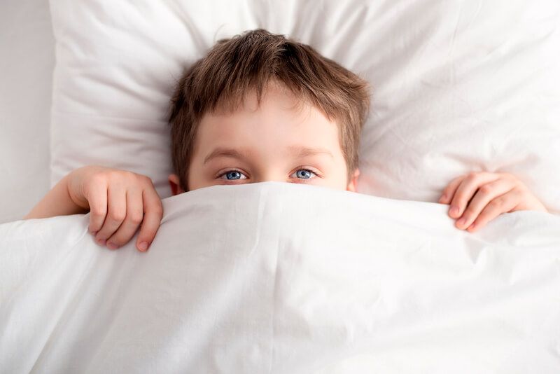 Little boy covering nose with bed sheet