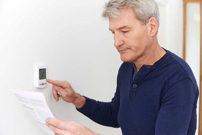 Man looking at paper while adjusting thermostat 